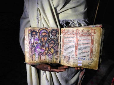 Priest holding ancient manuscript inside rock-hewn churches of Lalibela in Ethiopia